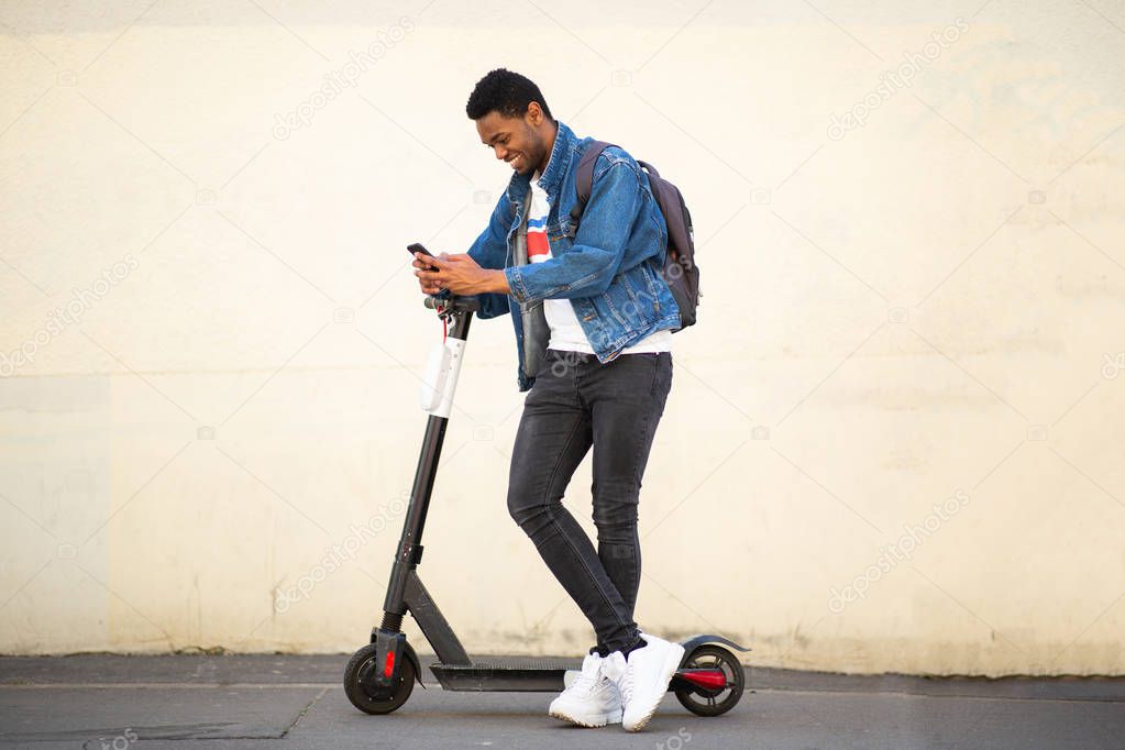 Full body portrait smiling african american man with mobile phone and scooter