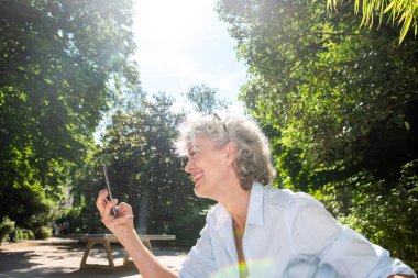 Cep telefonu iyon parkına bakan gülümseyen yaşlı kadının yan portresi.