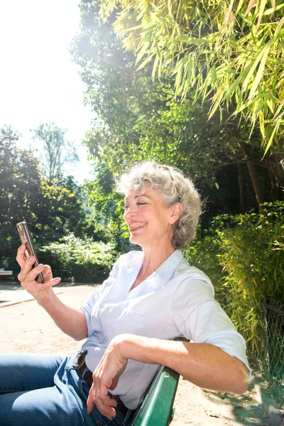 Портрет Пожилой Женщины Улыбающейся Сидящей Парке Смотрящей Мобильный Телефон — стоковое фото