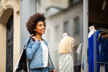 Afro-Amerikan kadın portresi mağazadan mağazaya kıyafet alışverişi yapıyor.