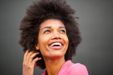 Güzel, genç, Afro-Amerikan bir kadının portresi. Gri duvara el ele gülüyor.