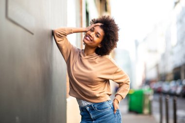 Dışarıda duvara yaslanmış afro saçlı mutlu bir zenci kadın portresi. 