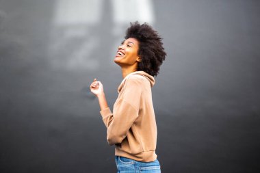 Gri duvarda kahkahalar atan afro saçlı çekici bir kadının yan portresi.