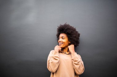Gri duvarda gülümseyen afro saçlı çekici siyah kadın portresi.