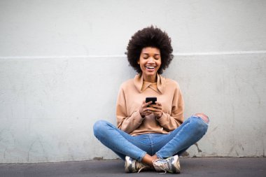 Cep telefonuyla yerde oturan mutlu Afro-Amerikan kadının portresi. 