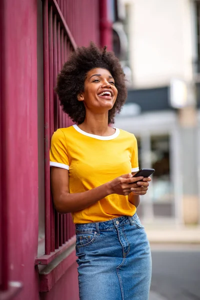 Portrait happy young african american woman holding cellphone outside in city