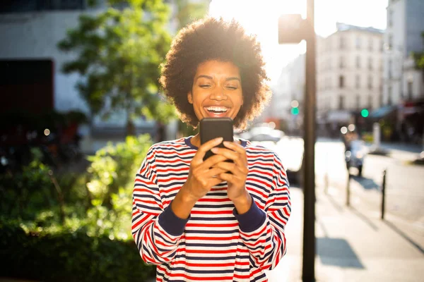 Portrait happy young black woman looking at mobile phone in city