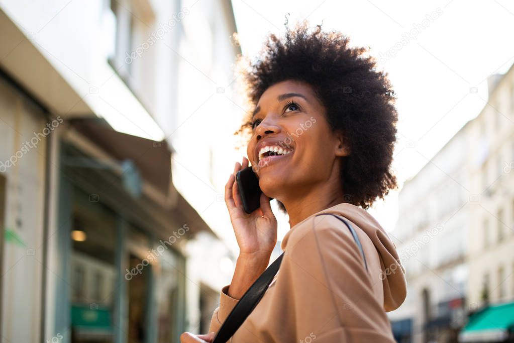 Side portrait of smiling young black woman talking with mobile phone in city