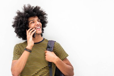 Çantalı mutlu genç adamın portresi ve izole beyaz arka planda cep telefonuyla konuşmak.