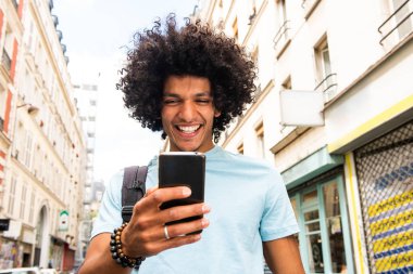 Portrait of smiling young man walking in city and looking at mobile phone