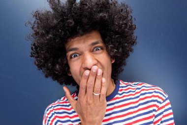 Afro saçlı ve eli ağzı kapalı şaşırmış genç adamın yakın portresi.