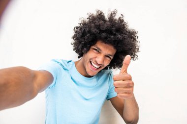 Portre mutlu genç Kuzey Afrikalı adam beyaz arka planda el işareti ile selfie çekiyor.