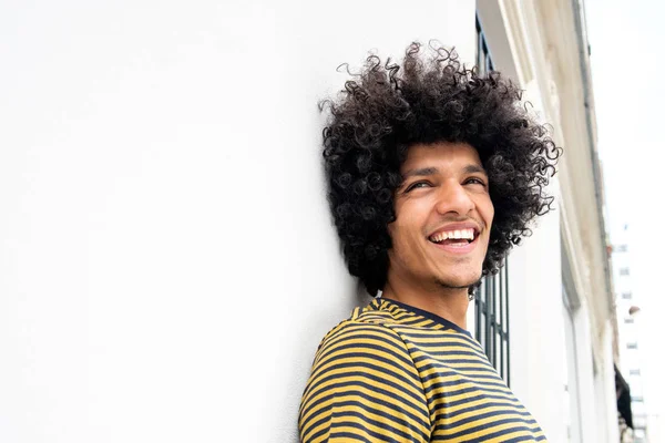 Side portrait of happy handsome young man leaning against white wall and laughing