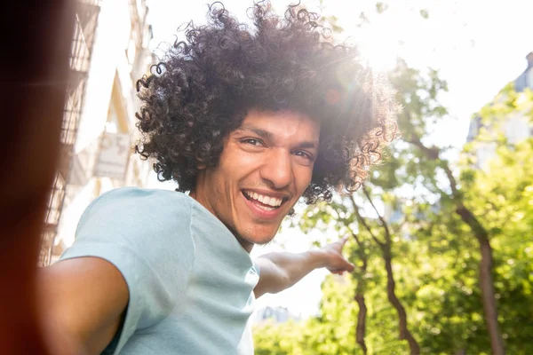 Portrait of smiling young North African man with afro hair taking selfie outside in city and pointing
