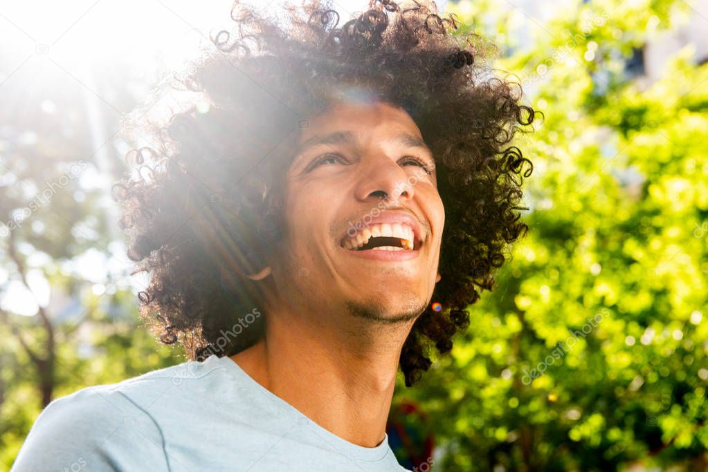 Close up portrait handsome young North African man with afro hair laughing outside 