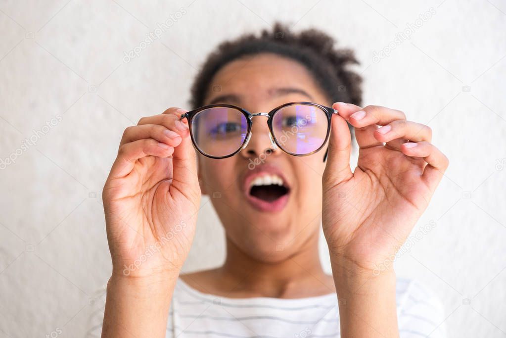 Close up portrait of young african american girl holding glasses making funny face by white wall