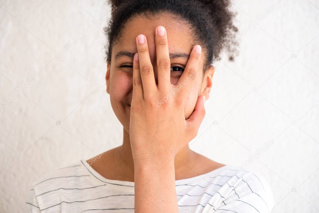 Portrait of cheerful young african american girl with hand covering face by white background