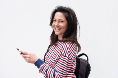 Cep telefonu ve çantasıyla beyaz arka planda gülümseyen genç bir kadının yan portresi 