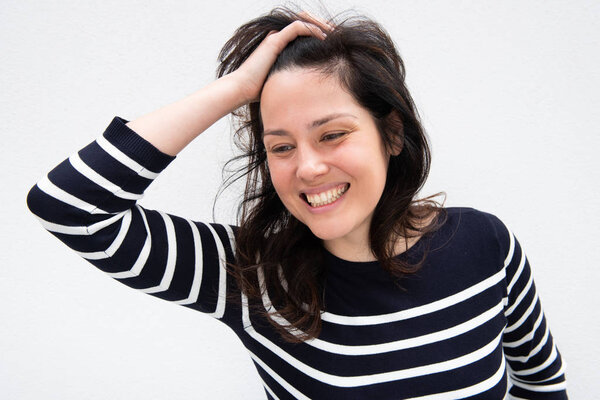 Portrait of happy young woman laughing with hand in hair by white background