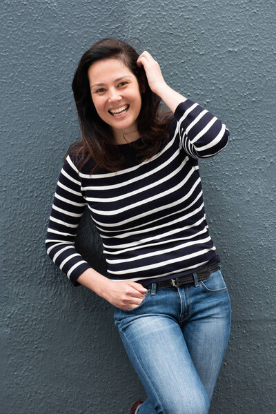 Portrait of young woman smiling by gray wall with hand in hair