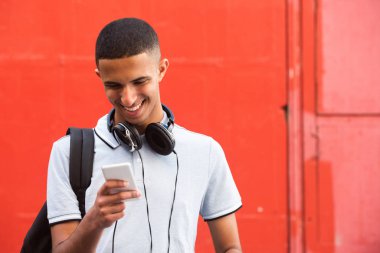 Kırmızı arka planda cep telefonuna bakan gülümseyen Arap genç adamın portresini kapat