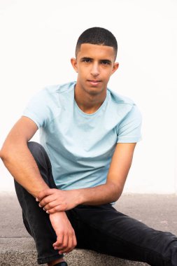 Yüzünde ciddi bir ifadeyle yerde oturan Arap bir gencin portresi.