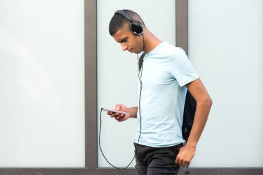 Cep telefonu ve kulaklıkla müzik dinleyen havalı bir gencin yan portresi