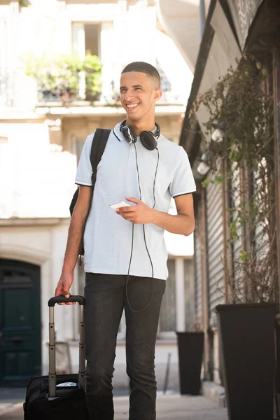 Porträtt Leende Ung Man Promenader Med Mobiltelefon Och Resväska Utanför — Stockfoto