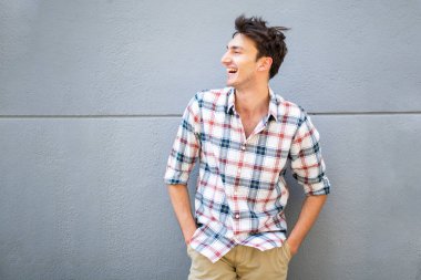 Gri duvarda poz veren ve gülen yakışıklı genç adamın portresi.