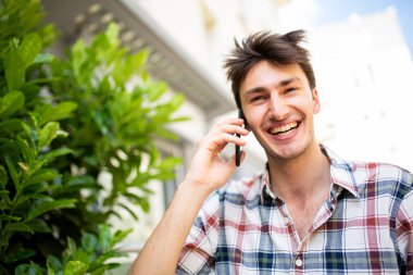 Dışarıda cep telefonuyla konuşan mutlu genç adamın portresini kapat.