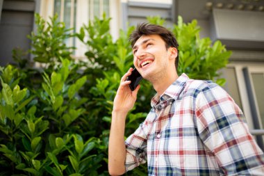Dışarıda cep telefonuyla konuşan neşeli bir gencin yan portresi.