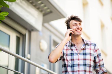 Portre mutlu genç adam dışarıda cep telefonuyla konuşuyor ve başka tarafa bakıyor.