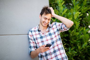 Elleri saçında gülümseyen ve dışarıdaki cep telefonuna bakan yakışıklı genç adam portresi.