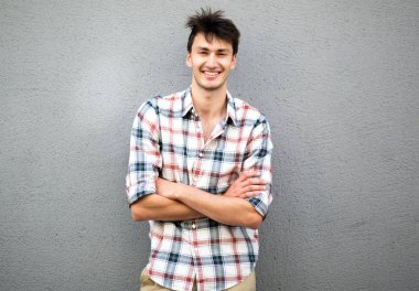 Gri arka planda kolları bağlı duran yakışıklı bir gencin portresi.