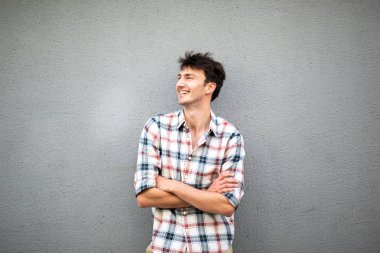 Portre yakışıklı genç adam gri arka planda duruyor kolları bağlı ve başka tarafa bakıyor.
