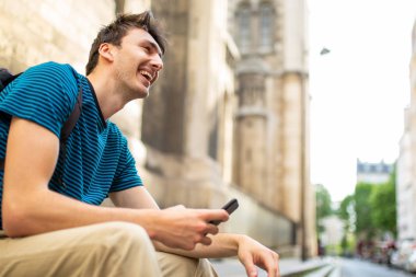 Dışarıda cep telefonuyla oturan mutlu genç adamın yan portresi.