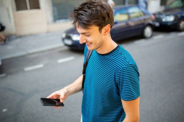 Sokakta cep telefonuyla yürüyen genç bir adamın portresi.