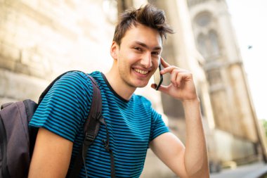 Şehrin dışında oturmuş telefonla konuşan mutlu bir gencin yan portresi.