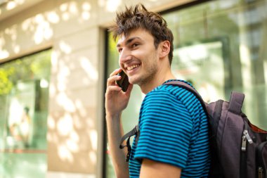 Şehirde cep telefonuyla konuşan erkek üniversite öğrencisinin yan portresini kapat.
