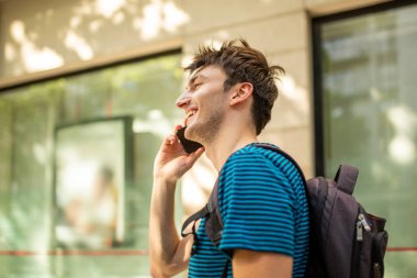 Şehirde cep telefonuyla konuşan mutlu bir gencin yan portresi.