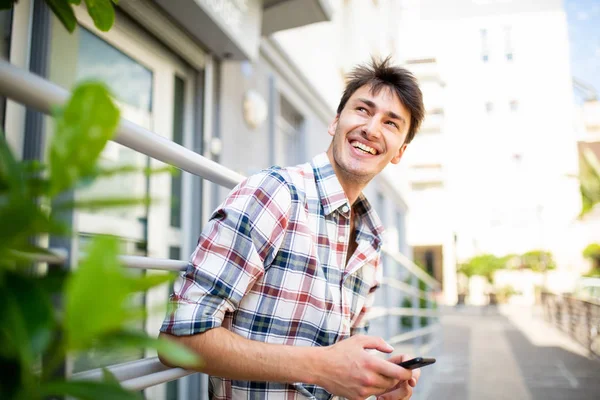 Side portrait of happy young man holding mobile phone outside