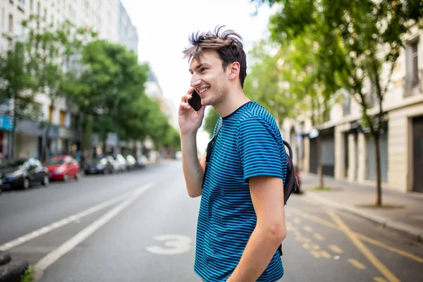 年轻人在与手机交谈时穿过街道的侧像 — 图库照片