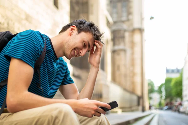 Боковой Портрет Улыбающегося Молодого Человека Сидящего Снаружи Смотрящего Мобильный Телефон — стоковое фото