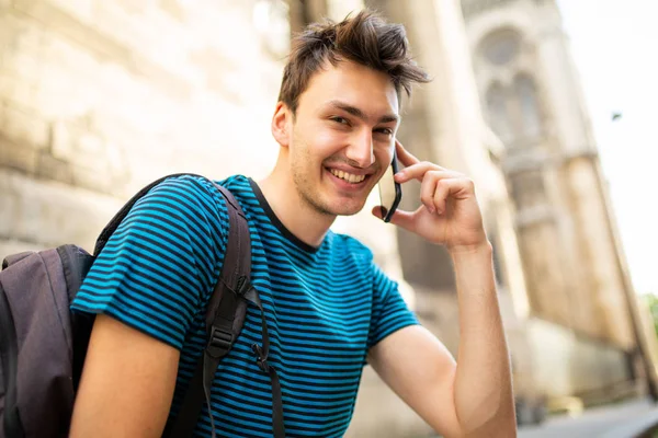 幸せな若い男のサイドポートレート外に座っている街で電話と話す — ストック写真