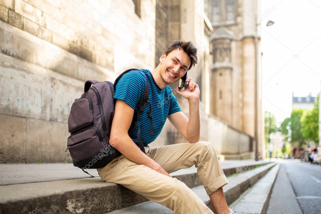 Side portrait of happy young man sitting outside in city talking with cellphone
