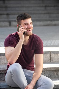 Dışarıda merdivenlerde oturan genç bir adam cep telefonuyla konuşuyor.