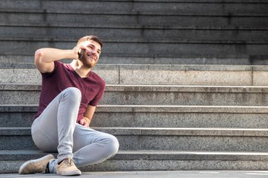Yakışıklı genç adamın vücut portresi basamaklarda oturuyor ve cep telefonuyla konuşuyor.