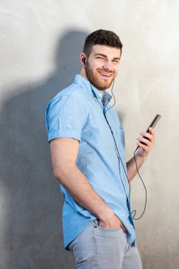 Cep telefonu ve kulaklıkla müzik dinleyen genç adam.. 