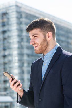 Şehirde cep telefonuyla gülümseyen iş adamının yan portresi