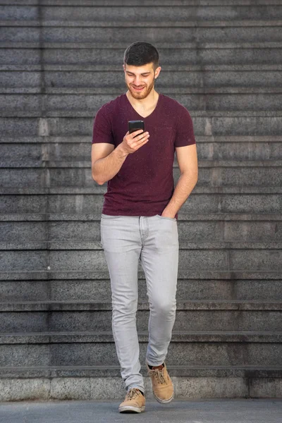 Cep telefonuyla yürüyen genç adamın tam boy portresi.